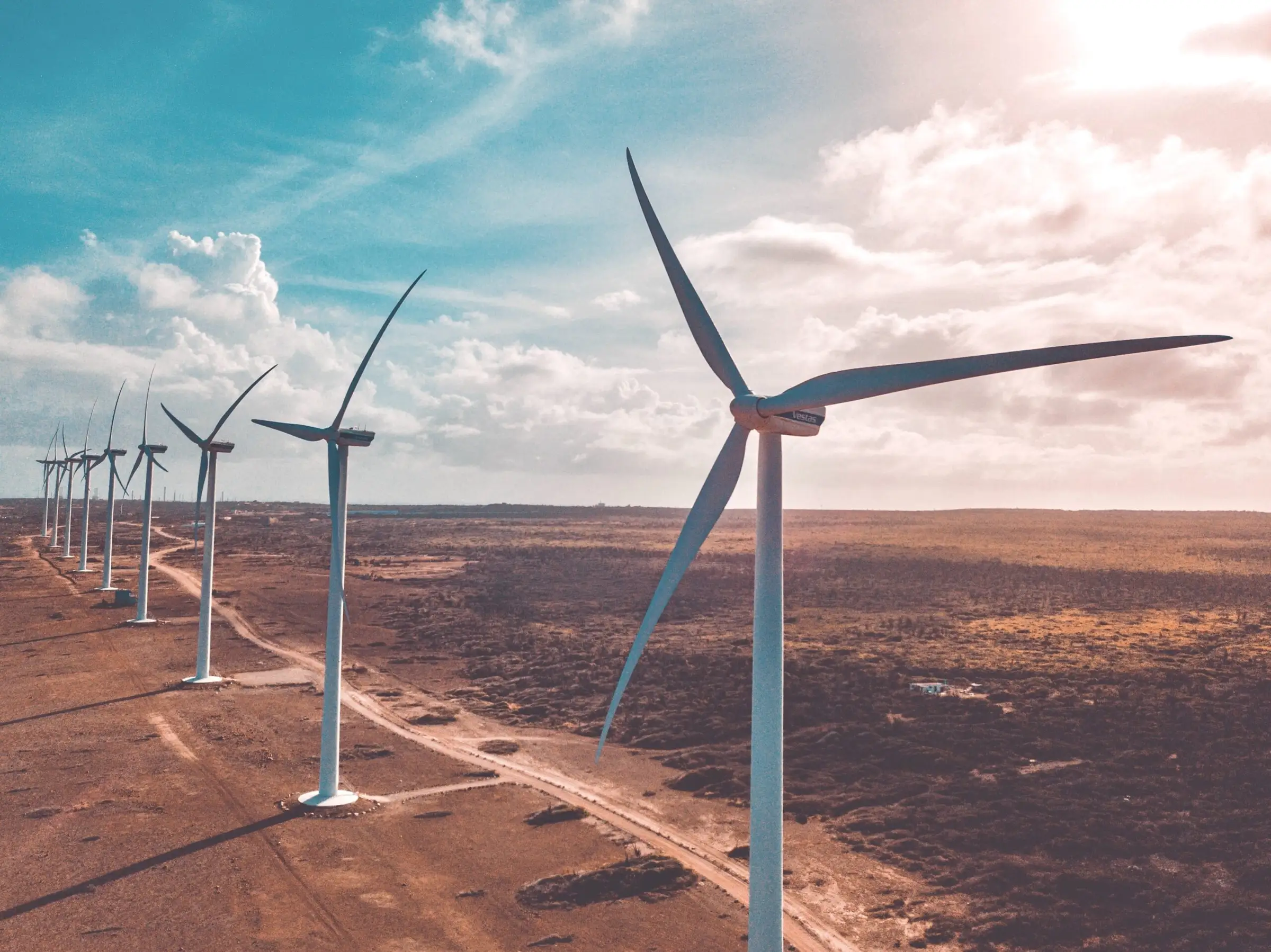 A line of wind turbines across dry open land under a hazy sky